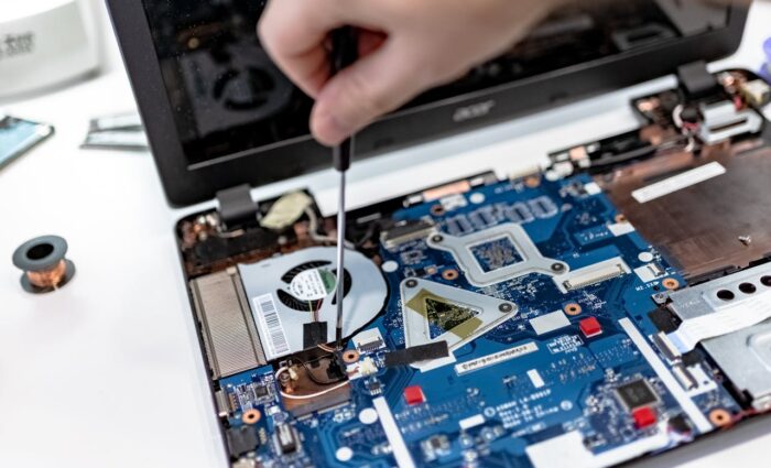 Technician diagnosing a laptop motherboard during repair at a local PC service center.