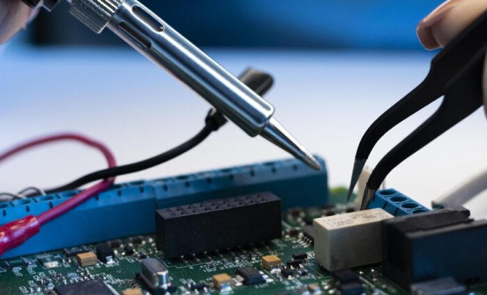 Technician repairing an open laptop motherboard using professional tools on a clean workbench.